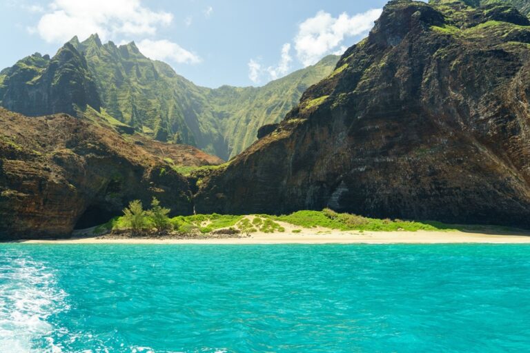 A stunning view of the Na Pali Coast in Kauai, Hawaii with turquoise waters and lush green mountains under a clear blue sky.