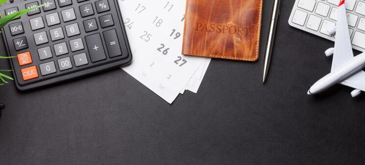 calculator, passport, keyboard, model airplane on desk.