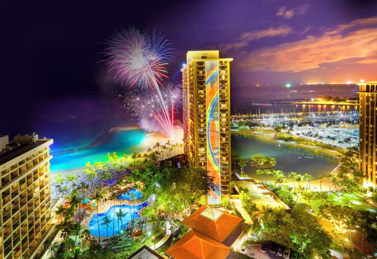 Night view of Hilton Hawaiian Village Rainbow Tower with fireworks in background.
