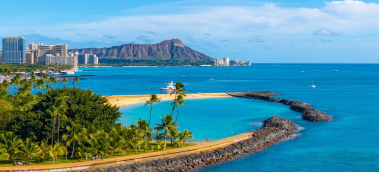 Aerial view of Oahu's Ala Moana Beach park, Waikiki and Diamond Head mountain in distance. blue ocean and palm trees.