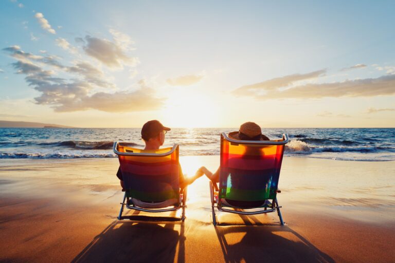 Silhouette of couple on lounge chairs on beach at sunset.
