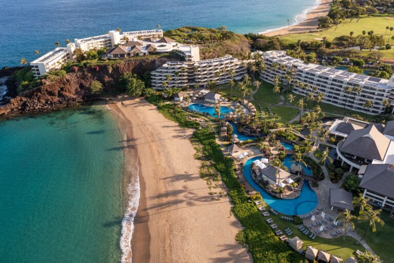 Aerial view of tropical resort with hotel, pools, and beach.