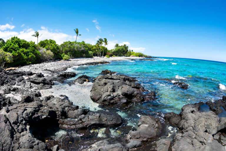 A beautiful black and white gravel beach with clear blue water on a remote beach in Kona Hawaii.