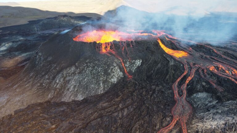 Red, yellow molten lava flowing out of volcanic crater, steam rising into sky